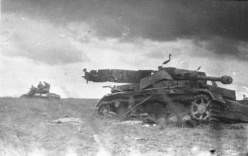 Уничтоженный немецкий средний танк Pz.Kpfw. IV на Курской дуге. На заднем плане удаляющийся советский легкий танк Т-70 с солдатами.