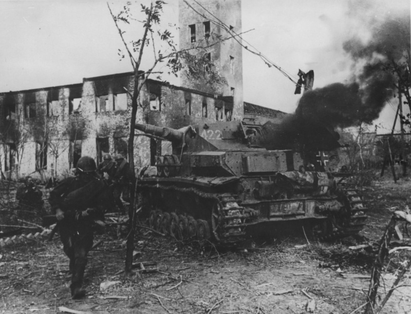 Советские солдаты передвигаются мимо дымящегося немецкого танка Pz.Kpfw. IV. в поселке Красноармейск (сейчас район Волгограда), около сталинградской судоверфи (завод № 264). Здание на фото — пожарная часть около проходной завода.