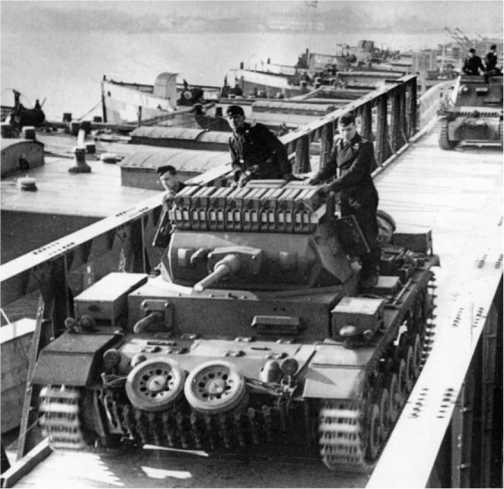 Pz.III Ausf.G проходит по мосту. Обращают на себя внимание способ усиления защиты лобовой части корпуса с помощью запасных гусениц и опорных катков, а также широко практиковавшийся в Вермахте способ перевозки 160 л топлива в канистрах на крыше башни.