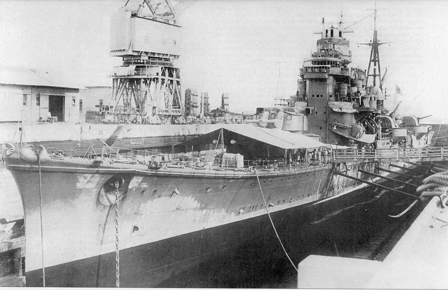 Крейсер «Ашигара» в большом сухом боке короля Георга VI на военно-морской базе Селетар в Сингапуре, 31 декабря 1942 г. Крейсер заведен в док на текущий ремонт и окраску подводной части. На снимке отлично видны стремительные обводы корпуса крейсера. Обратите внимание на наделку по периметру корпуса у самого его среза — здесь уложены кабели размагничивания, исключавшие срабатывание магнитных мин — характерная особенность всех японских крейсеров. На крыше надстройки установлен оптический дальномер централизованной системы управления стрельбой артиллерии главного калибра. Дальномер в целях быстрого опознавания корабля окрашен в белый цвет. В ходе модернизации 30-х годов к корпусу крейсера были приделаны були для увеличения остойчивости корабля и улучшения его защищенности от торпед. Буль левого борта виден ни снимке, ниже ватерлинии.