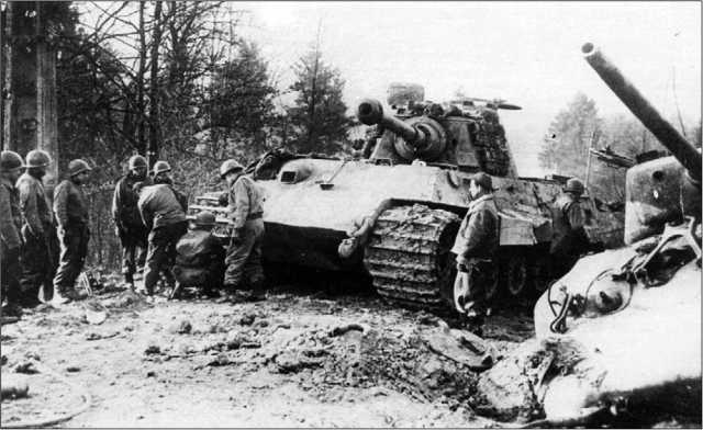 Американские солдаты осматривают поврежденный и оставленный экипажем «Королевский тигр». На переднем плане справа — подбитый «Шерман» М4А1. Германия, весна 1945 года.