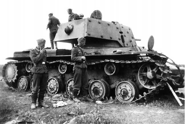 Немцы осматривают подбитый танк КВ-1 с экранированной башней. Машина имеет усиленные опорные катки: два передних без отверстий в ободе, остальные с дополнительными ребрами жесткости. Машина из состава <a href='https://arsenal-info.ru/b/book/348132256/10' target='_self'>танкового батальона</a> Лужской оперативной группы была подбита 16 июля 1941 года (АСКМ).